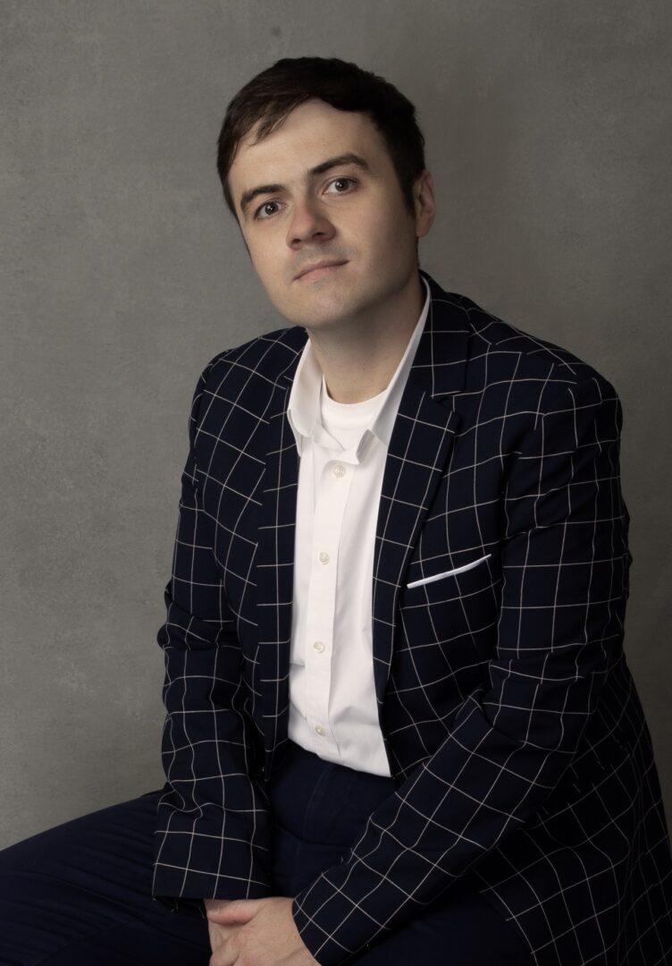 Man in checkered suit sitting, gray background.