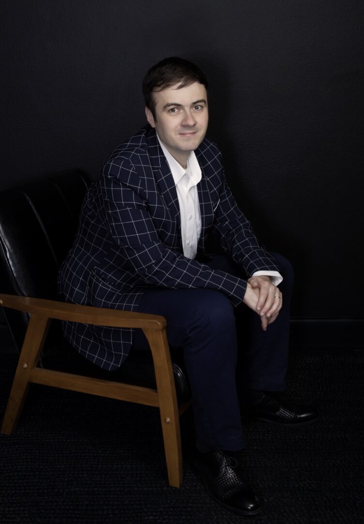 Man sitting on chair in checkered suit.